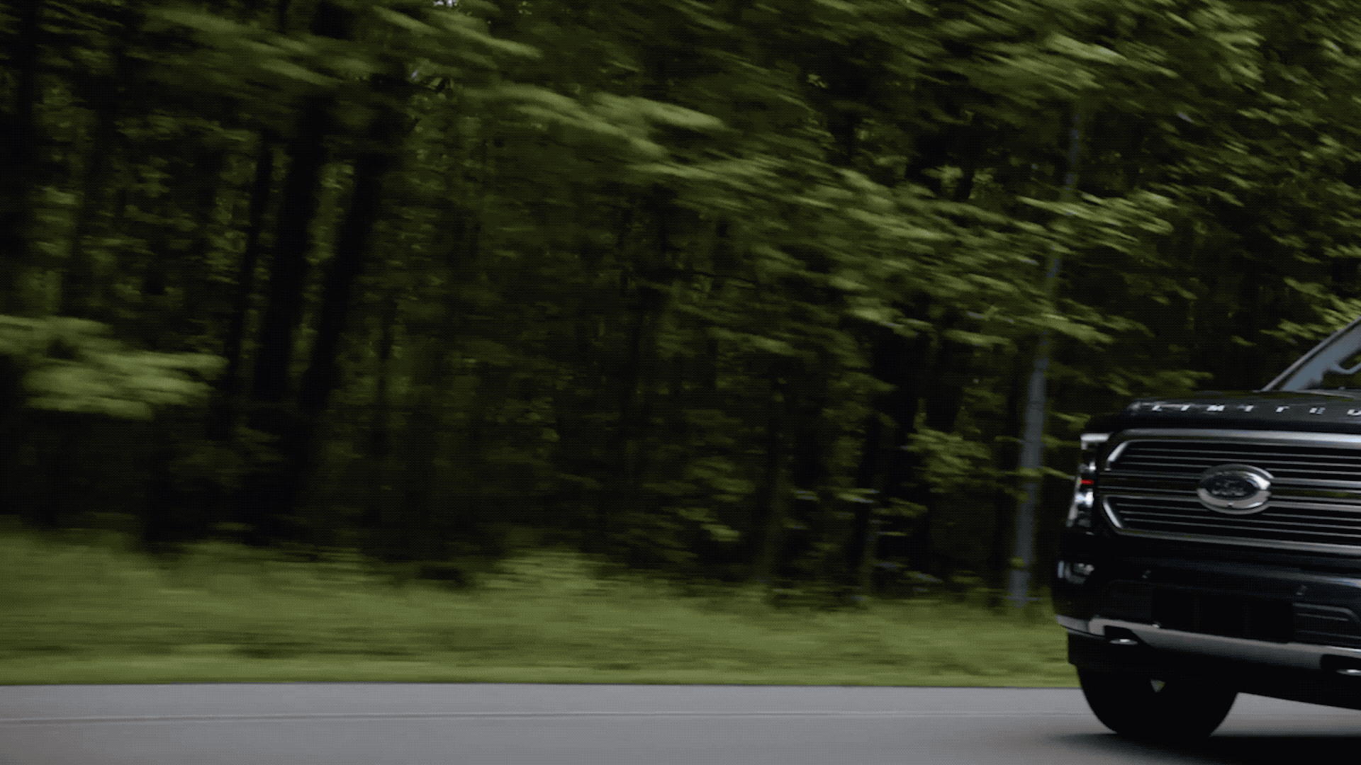 A black pickup truck drives along a forested road.