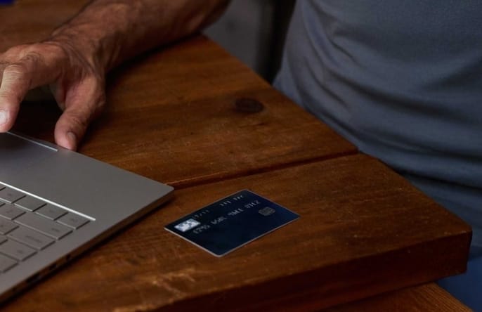 A person uses a laptop on a wooden table with a credit card placed nearby.