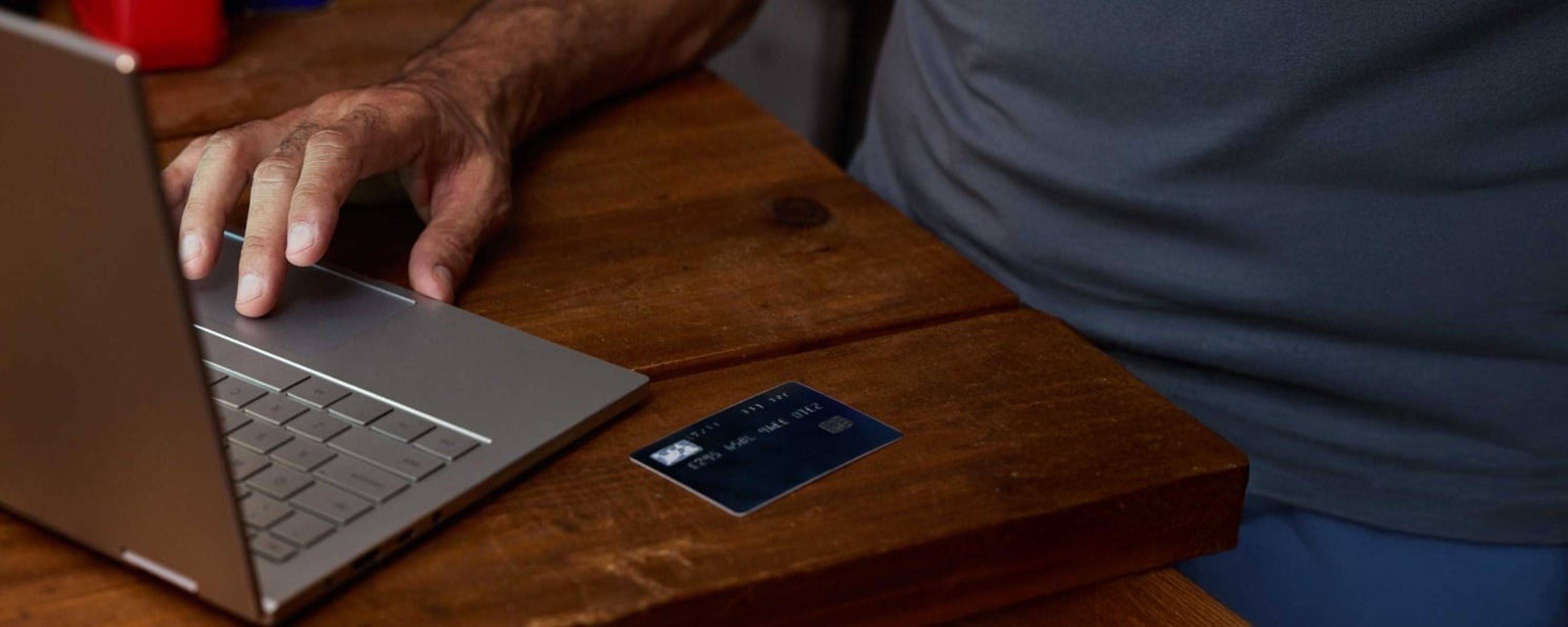 A person uses a laptop on a wooden table with a credit card placed nearby.