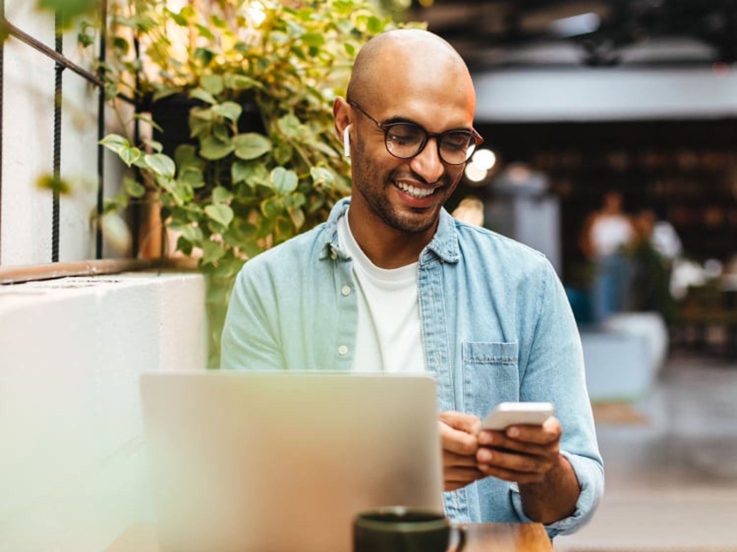 Image of a man using his cellphone while working on a laptop at a cafe table