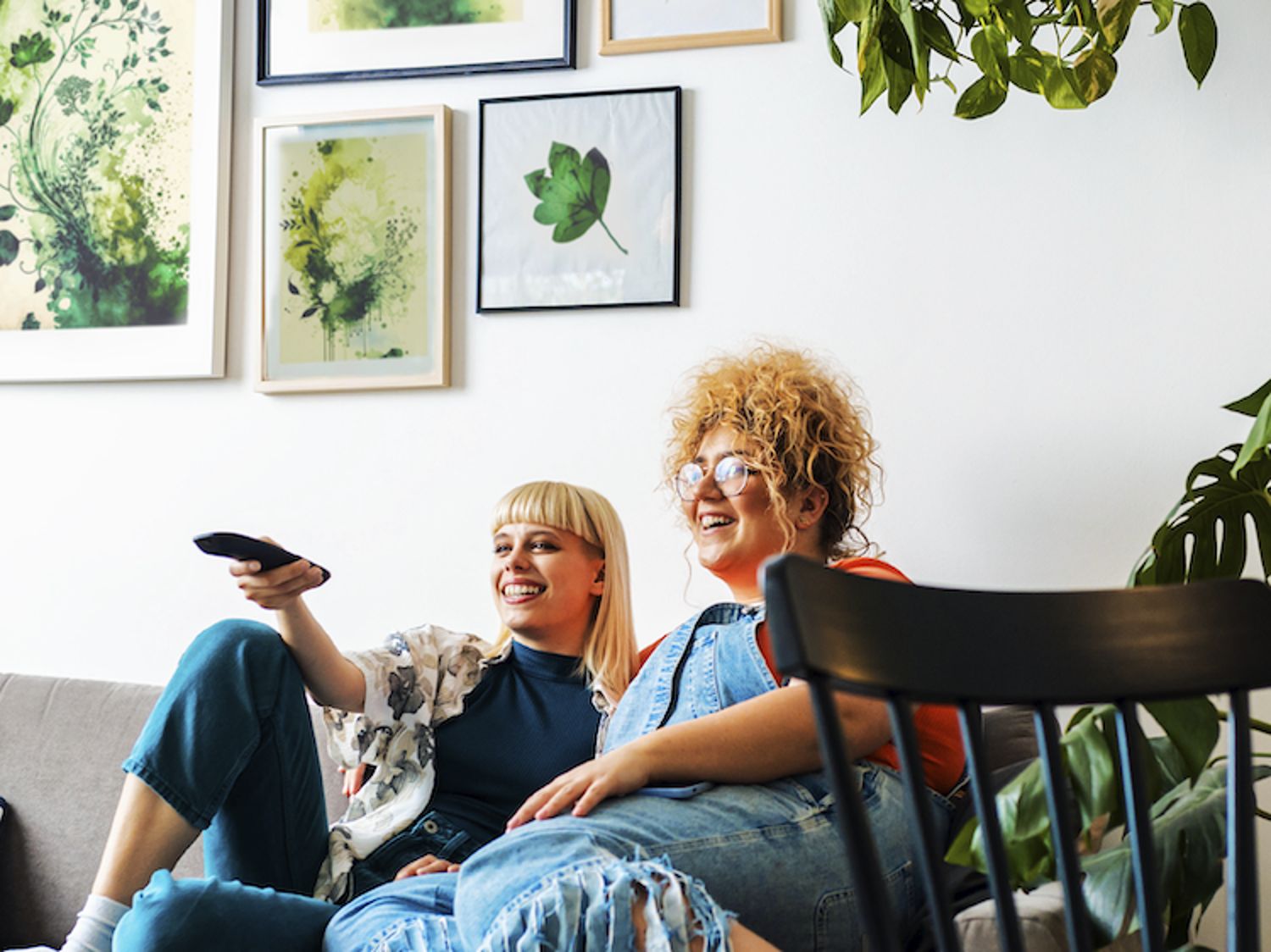 Photo pictures a couple on a couch watching TV and laughing