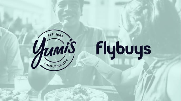 Two people share nachos and drinks at an outdoor table, overlaid with the Yumi's Family Recipe logo on the left and the Flybuys logo on the right.