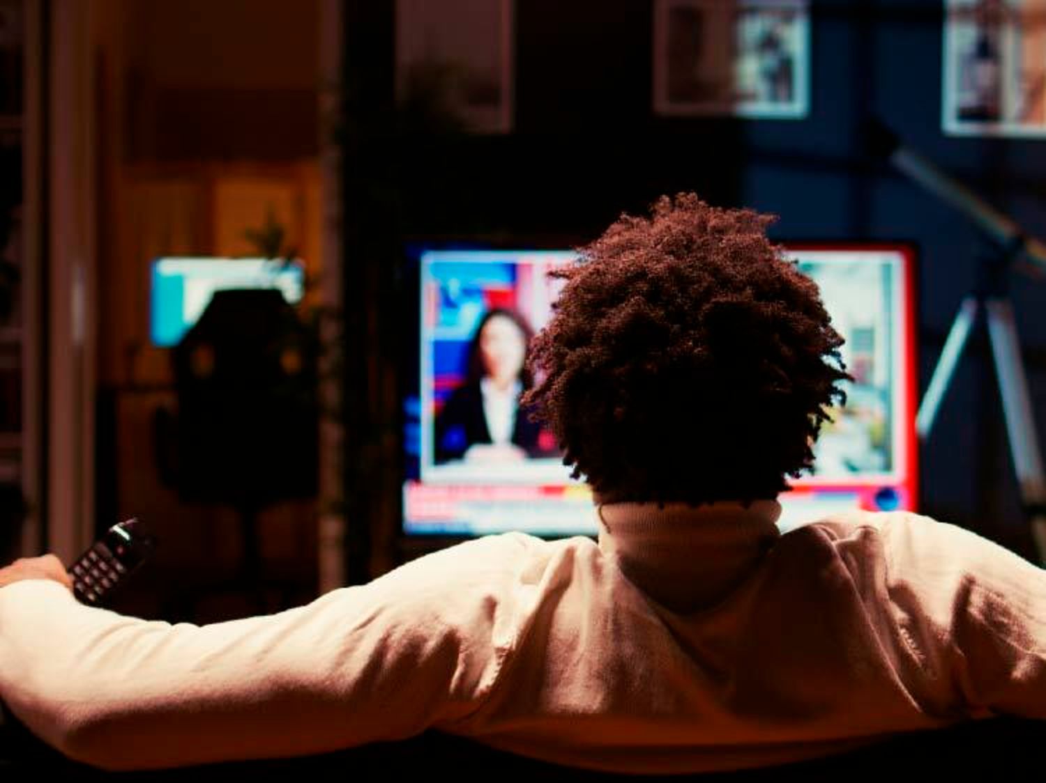 Image shows the back of a person's head while they watch television