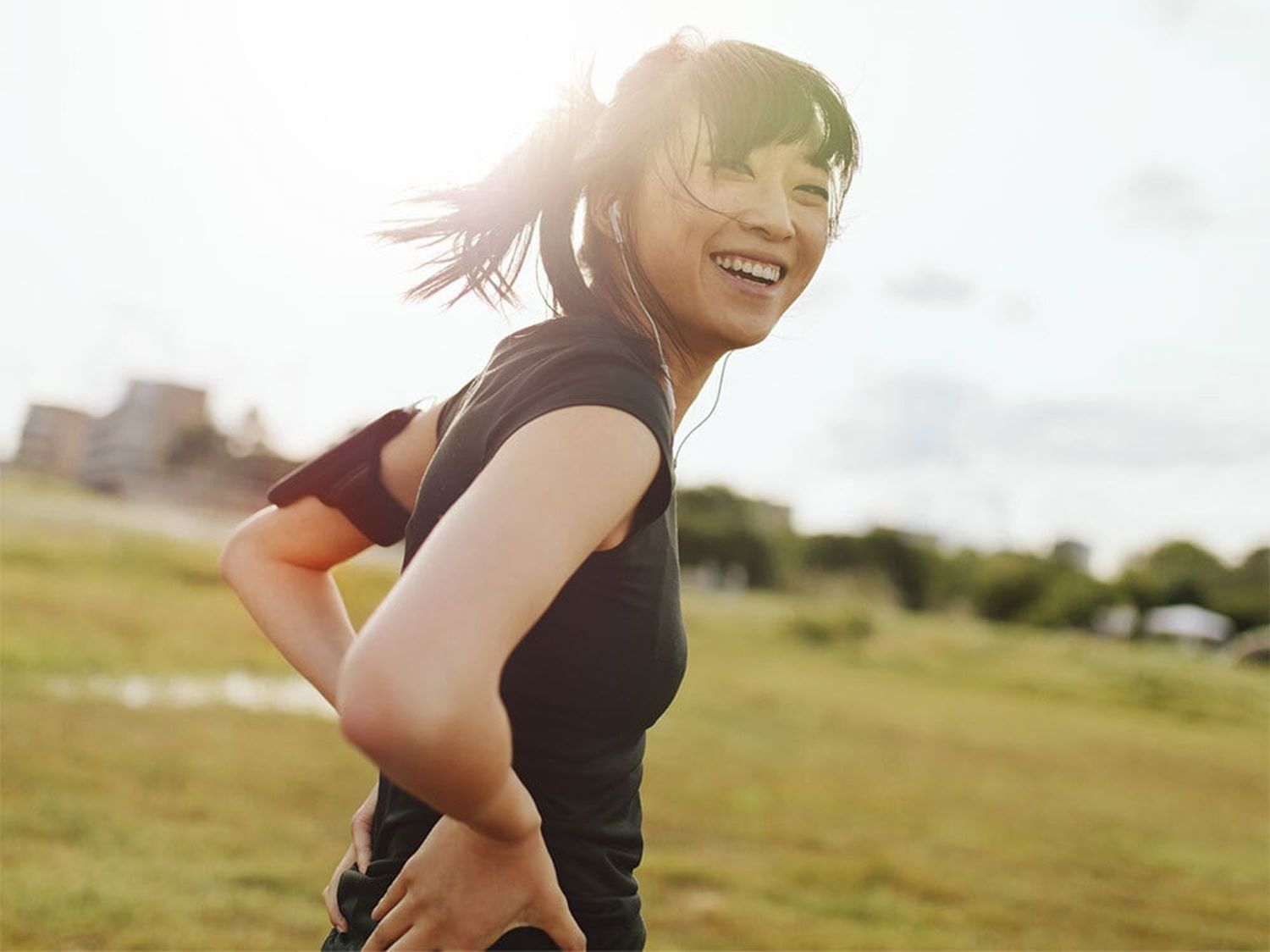 Person running outdoors in a grassy field with sunlight in the background.