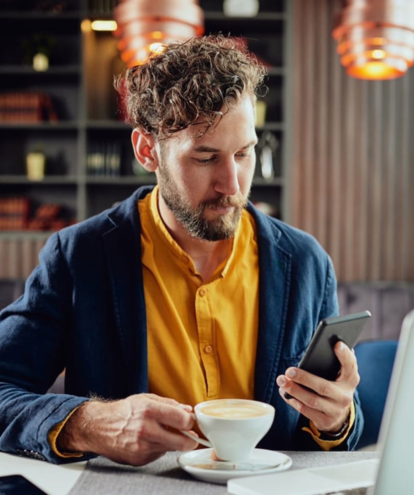 Man sitting in a stylish café, sipping coffee while checking his smartphone in a relaxed setting