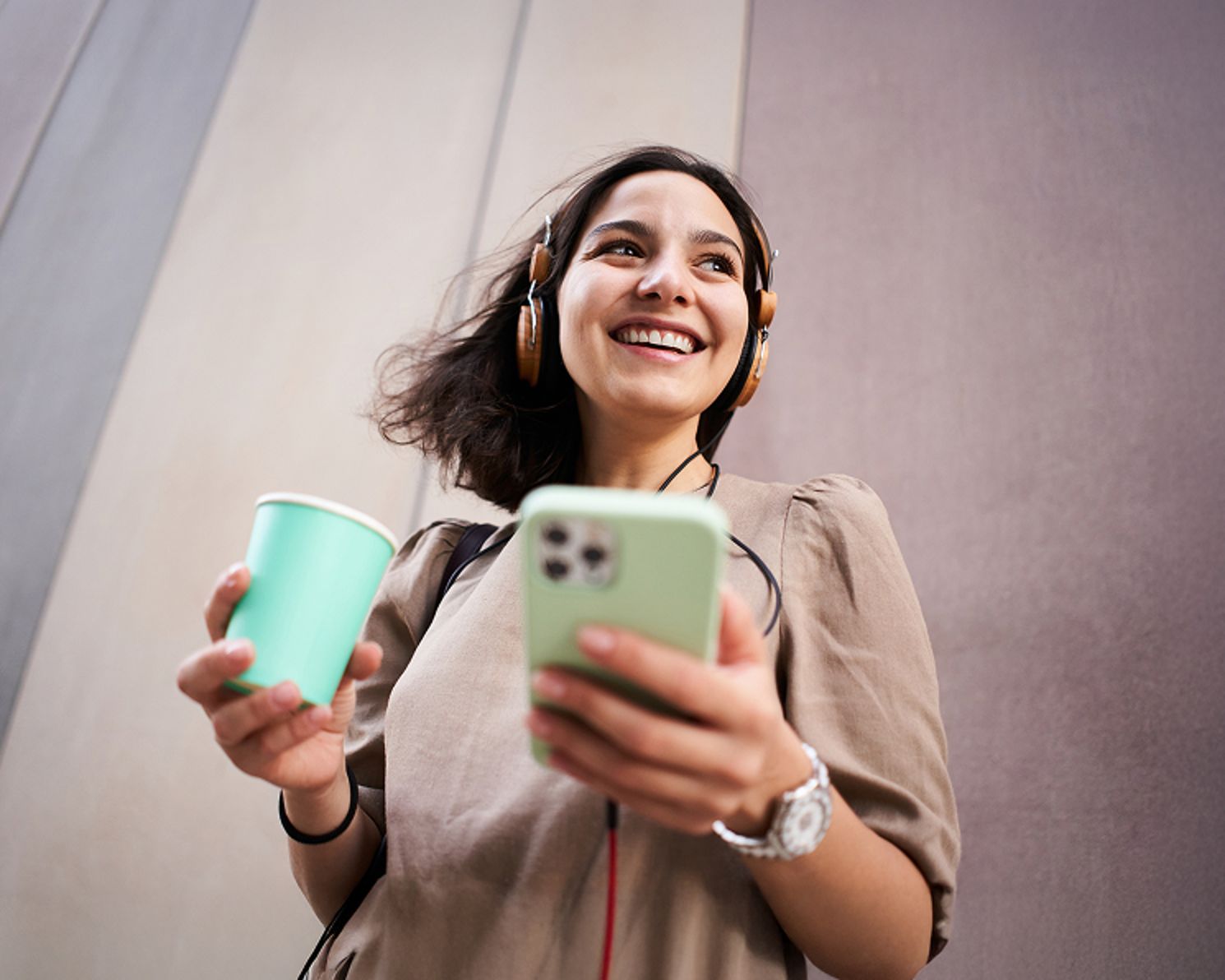 Woman wearing headphones and holding a cup of coffee in one hand and her phone in the other
