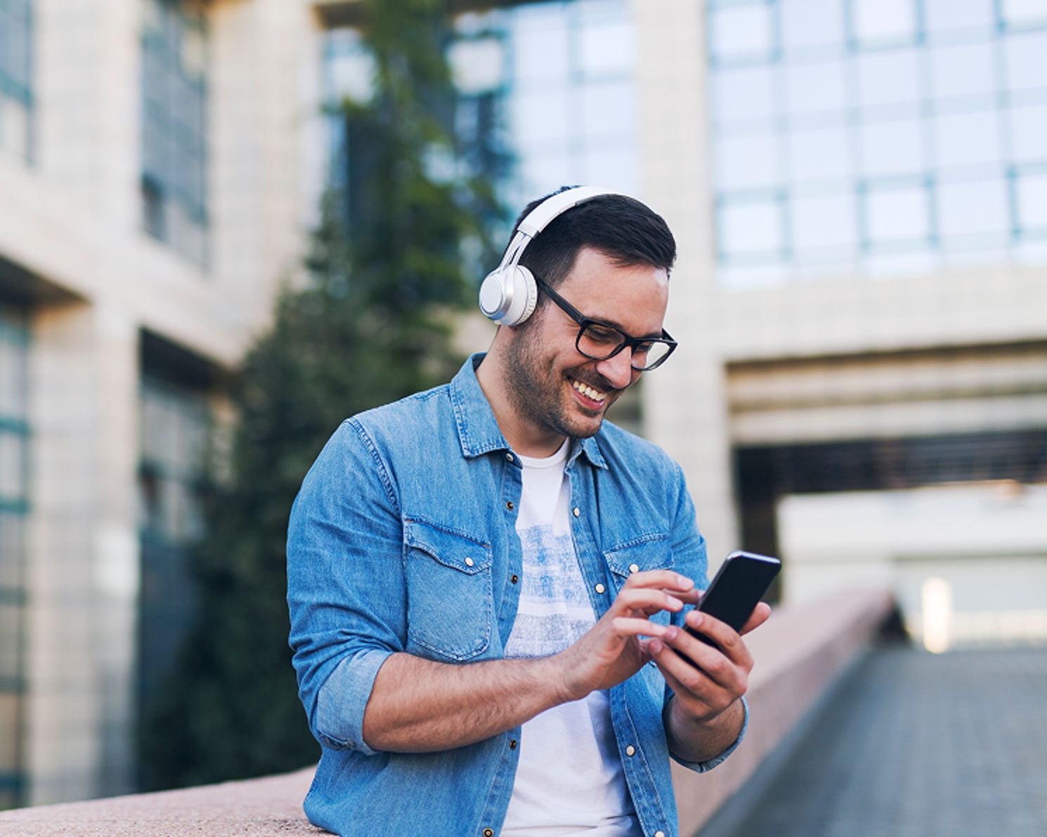Man wearing headphones and looking at his phone while smiling