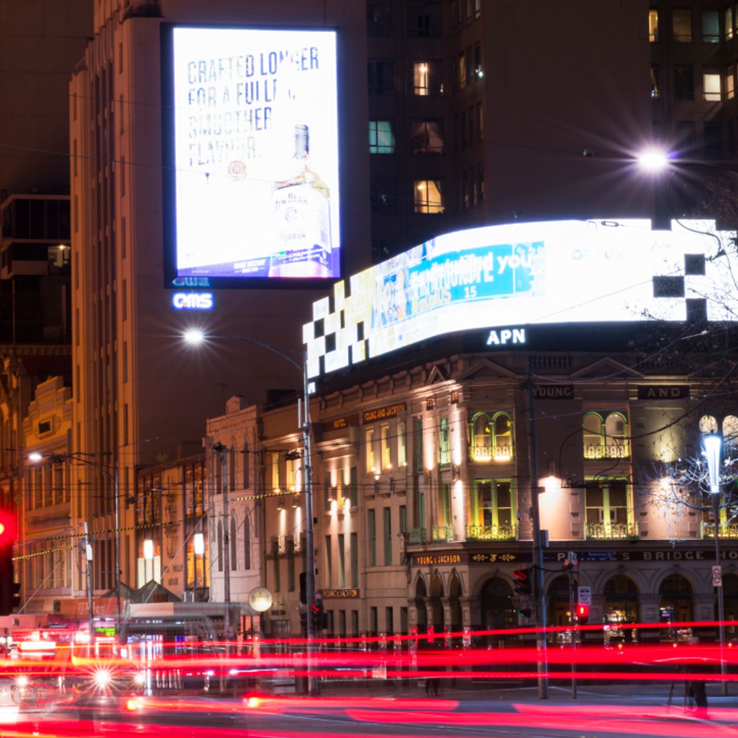Un paisaje nocturno con grandes vallas publicitarias digitales que iluminan una ajetreada calle y capturan la energía de la publicidad exterior digital en un entorno urbano.