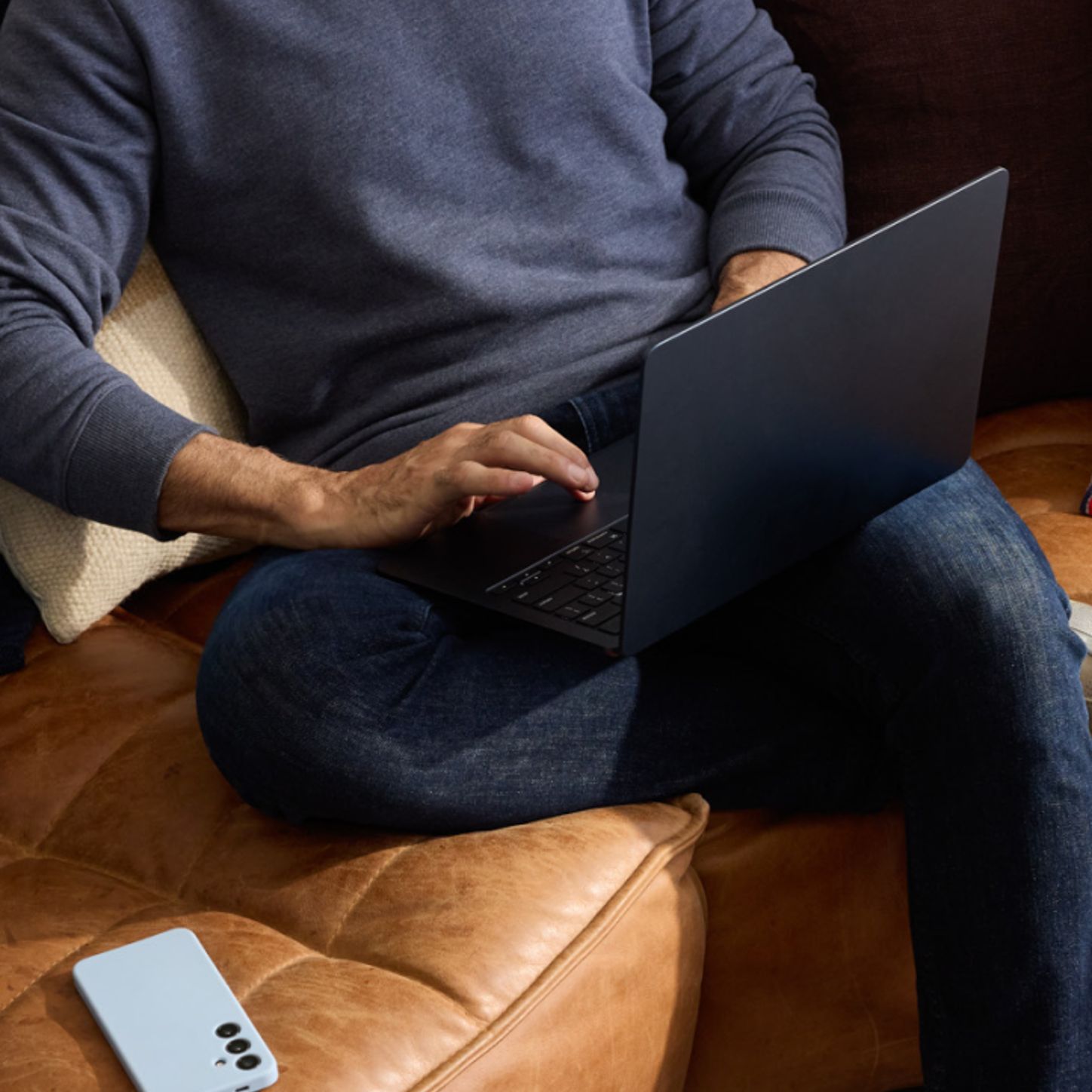 Hay persona sentada cómodamente en un sofá de cuero con un portátil y un smartphone cerca, y esto transmite un entorno de trabajo o de investigación relajado y tecnológico.—