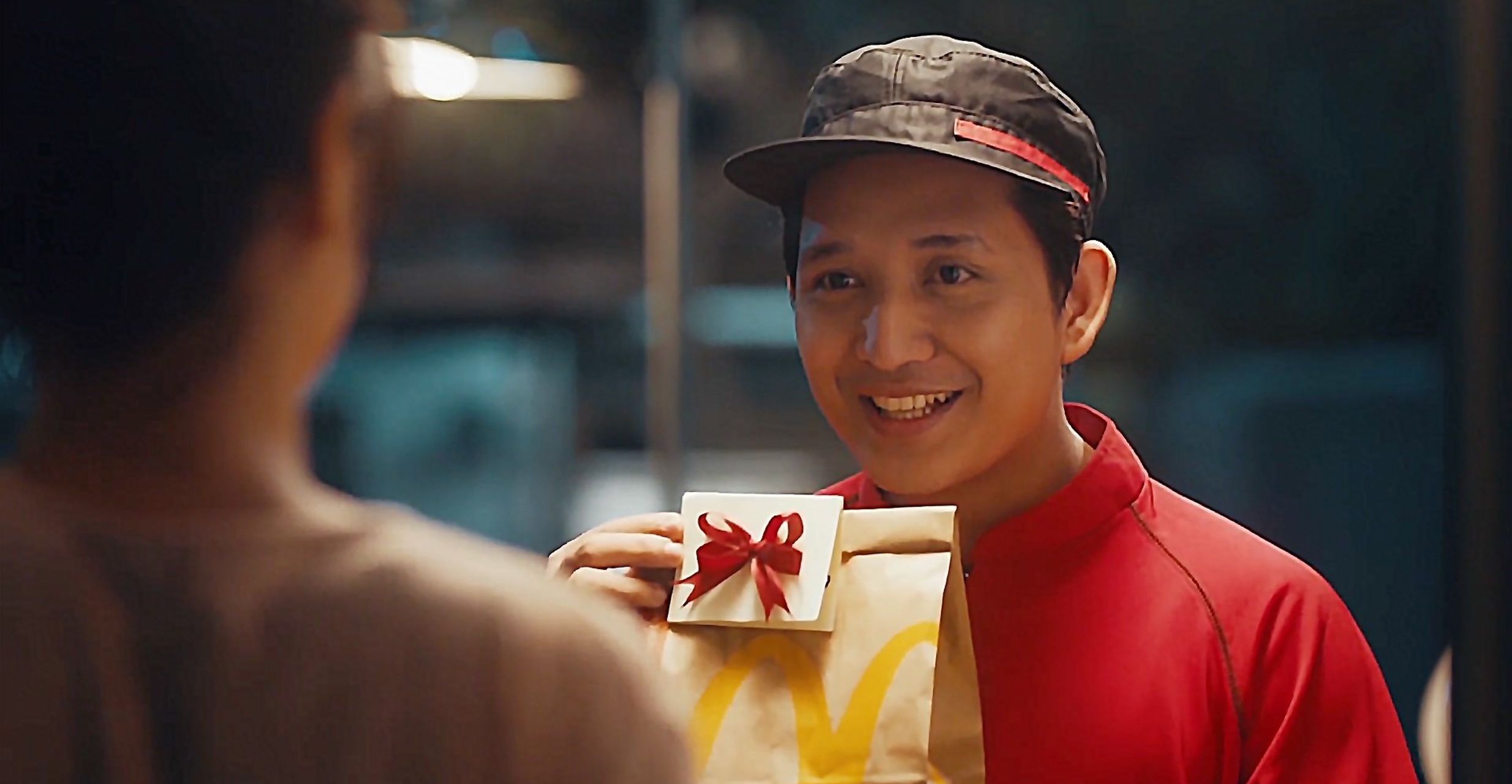 A smiling delivery person hands over a gift-wrapped food package to a customer.