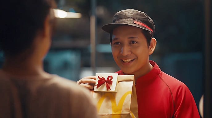 A smiling delivery person hands over a gift-wrapped food package to a customer.