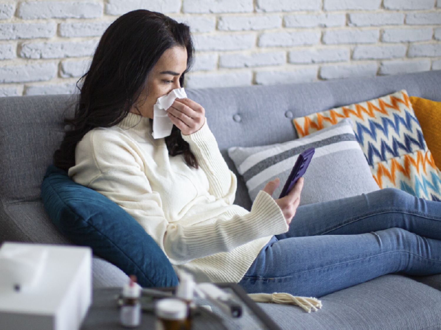 Woman sitting on sofa and blowing her nose into a tissue