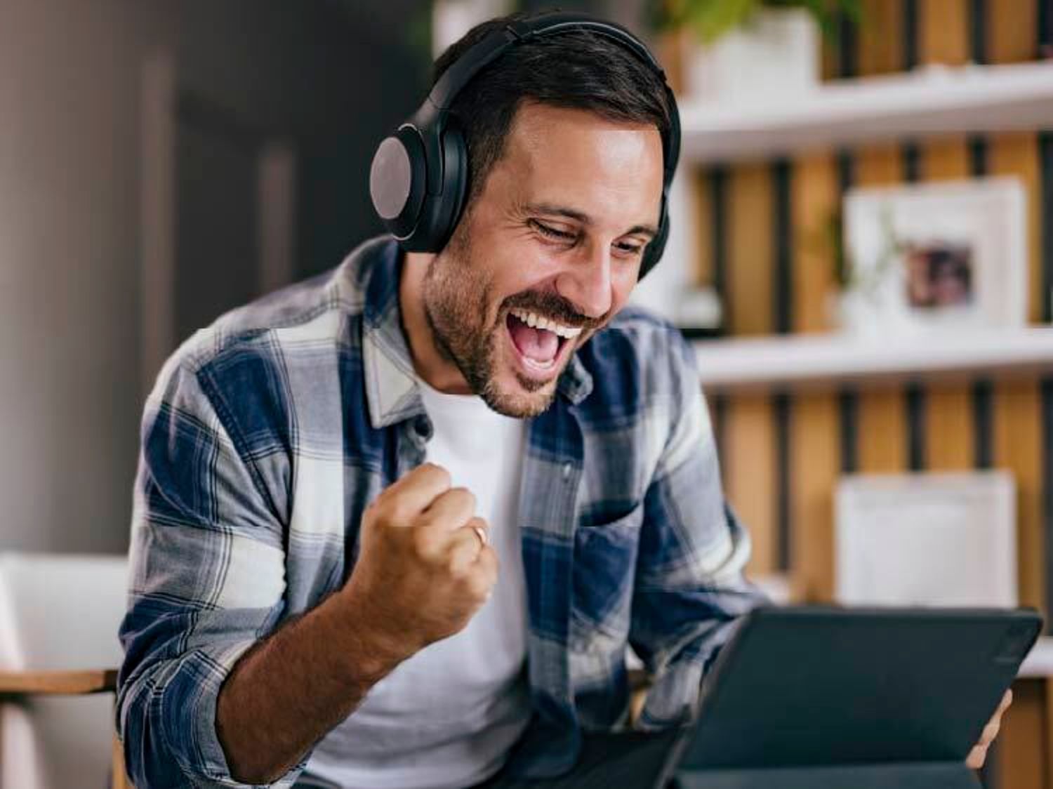 Man cheering while looking at a laptop and wearing headphones