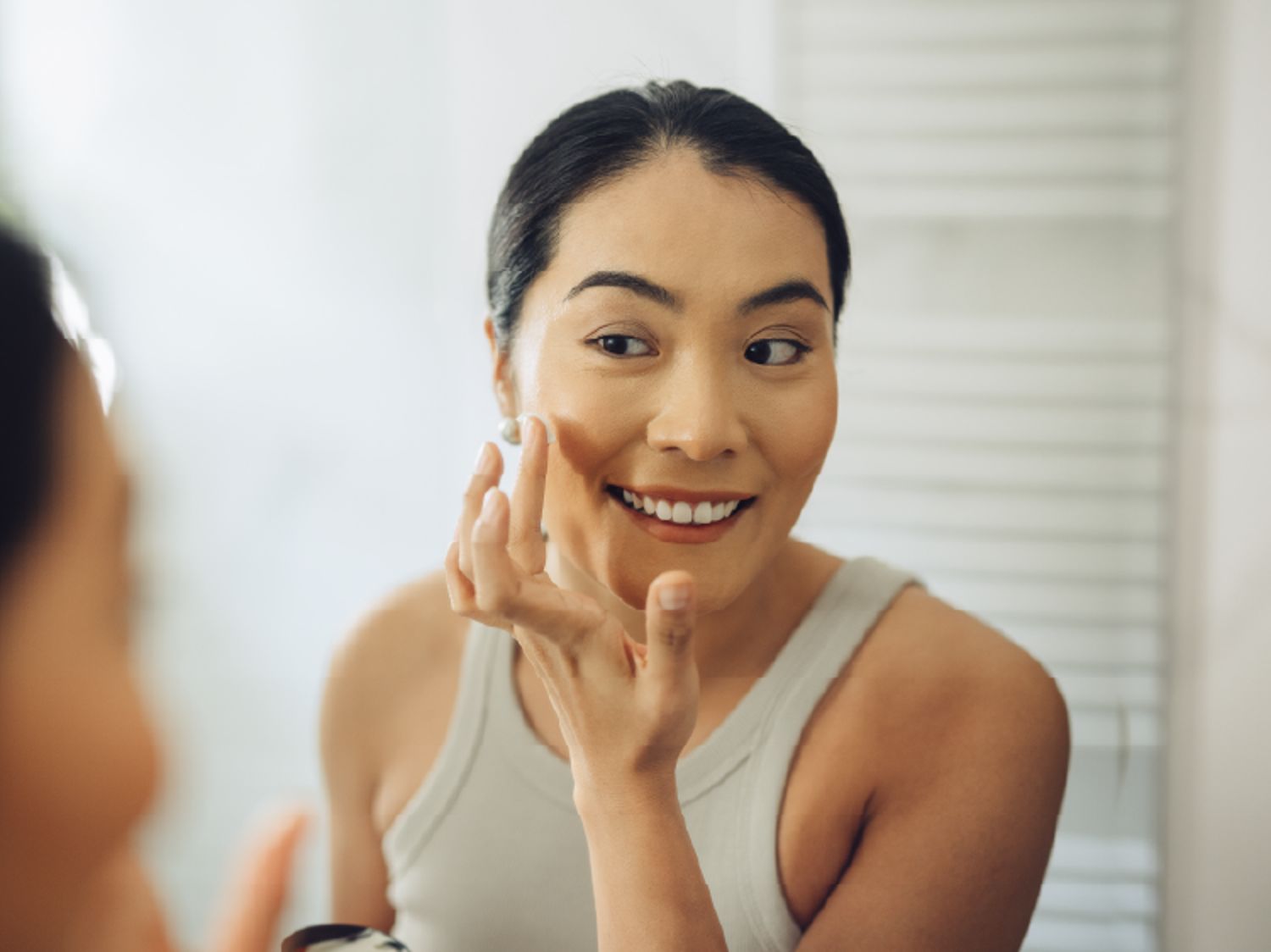 Woman looking in the mirror and smiling, while doing her skincare.