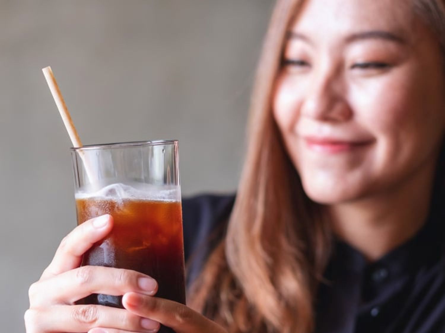 A woman smiles while holding a glass of cola with a paper straw.