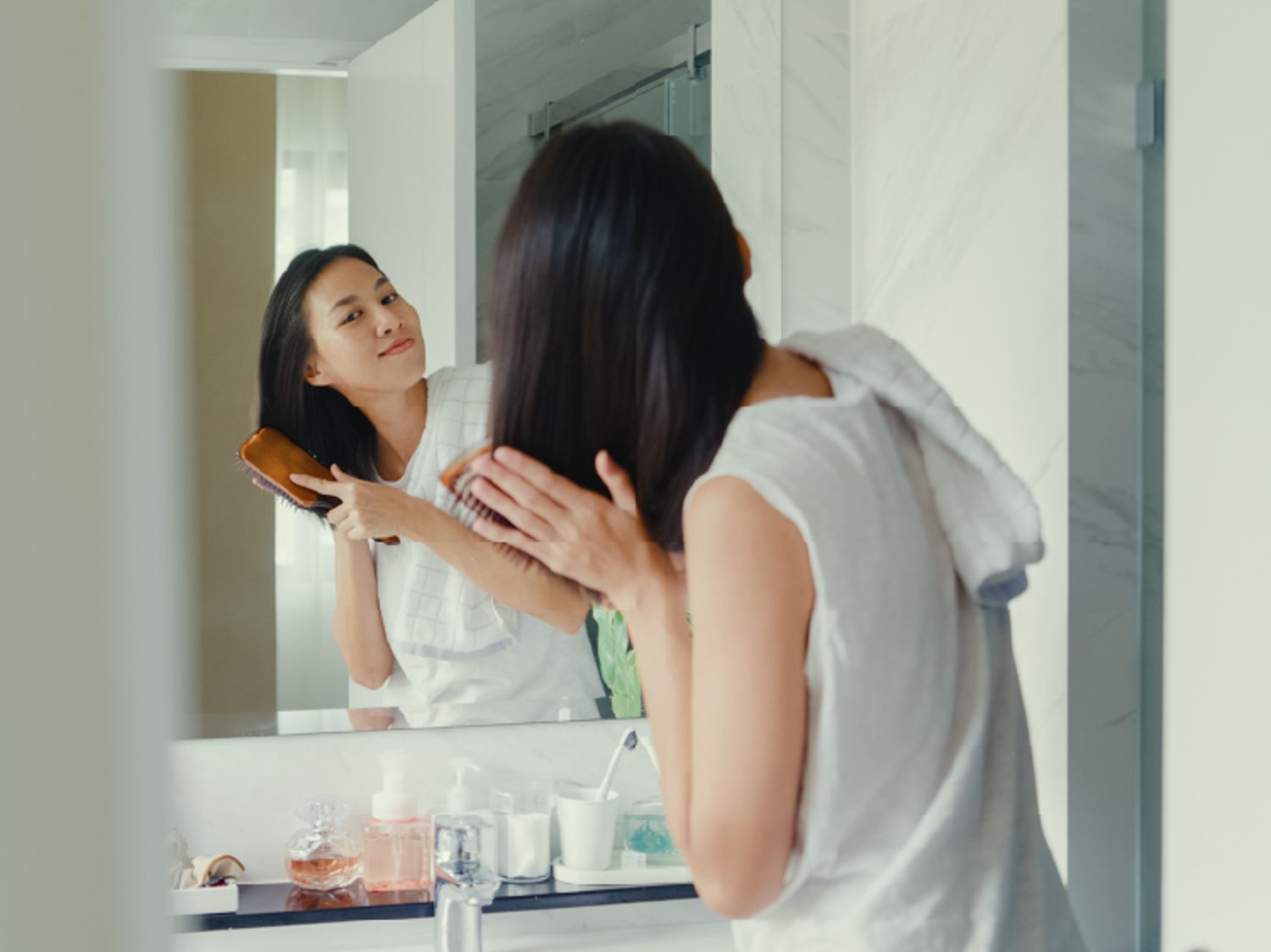 Image shows a person brushing their hair before a bathroom mirror