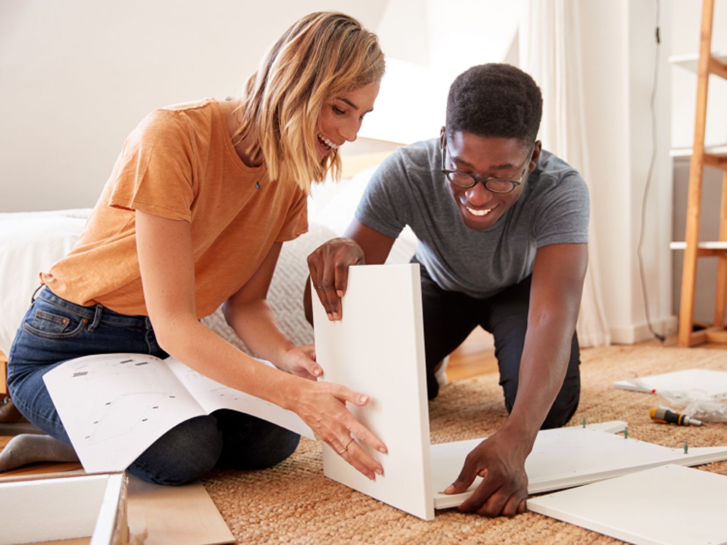 Smiling couple assembling furniture together on the floor of a bright living room