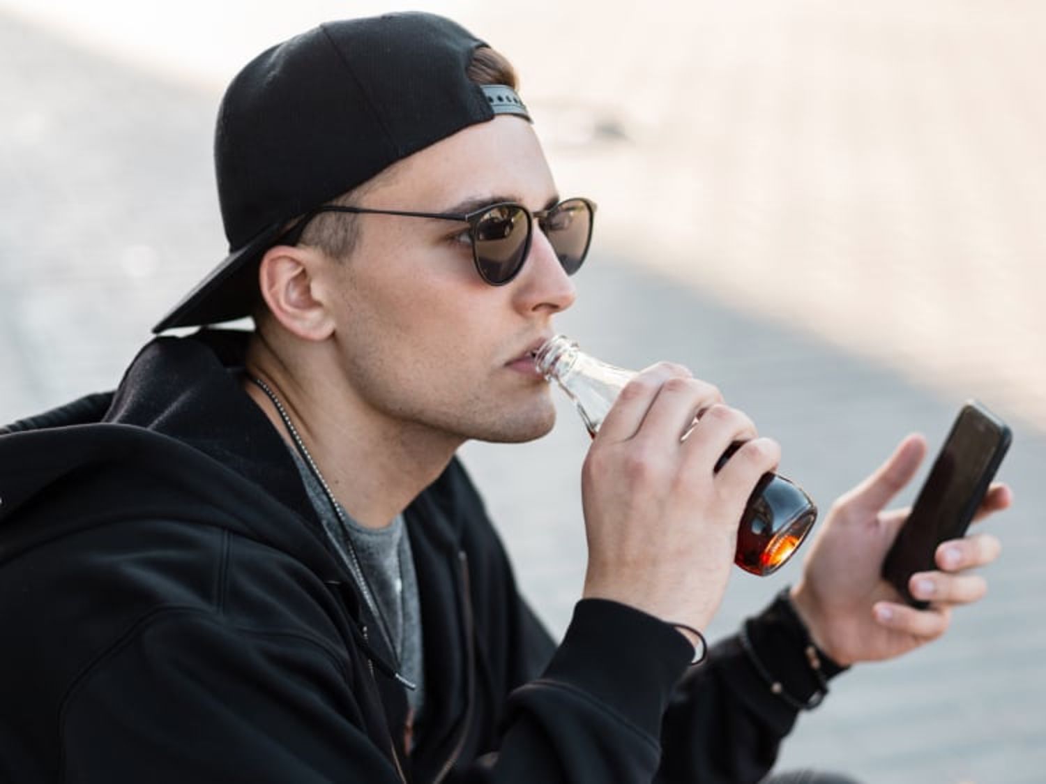 Image shows man sipping from a Pepsi bottle with his phone in hand