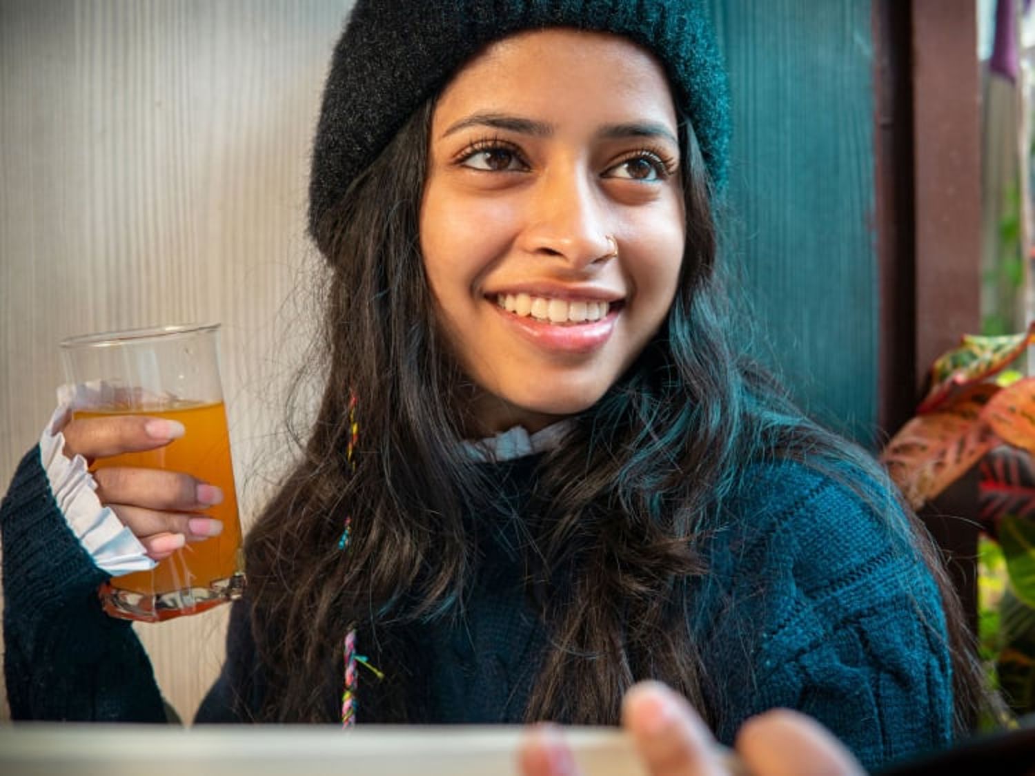 Woman in a beanie, holding a juice and looking away while smiling