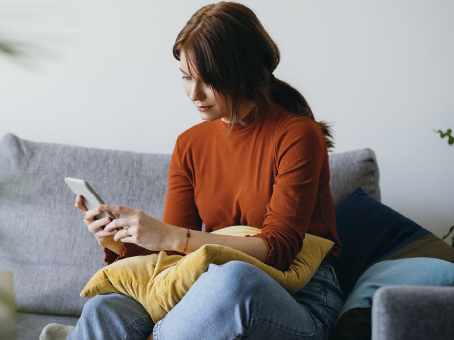 Person sitting on a couch holding a smartphone with a yellow cushion in the background