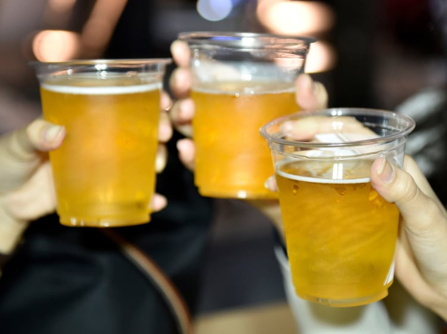 Image shows three hands holding three cups of beer