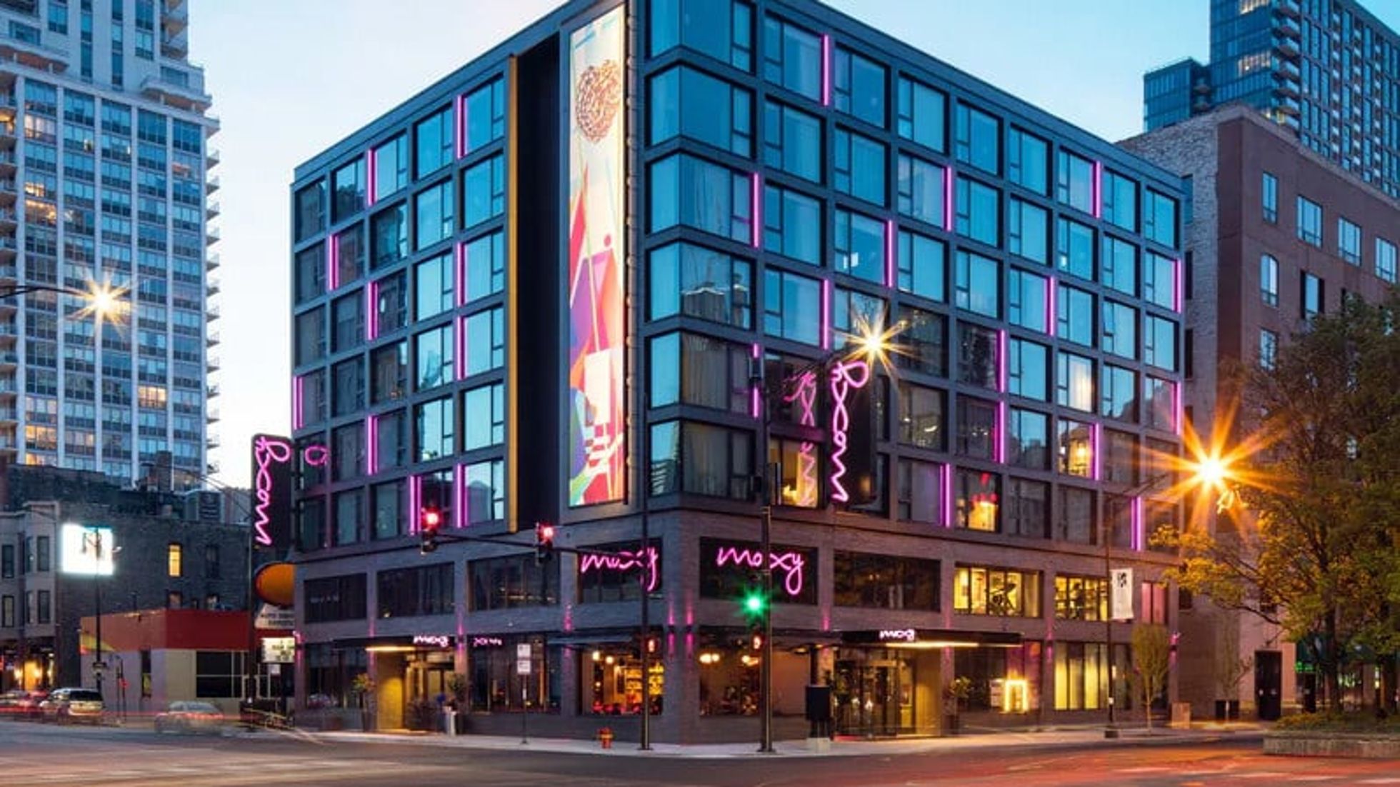 Modern hotel building with glass windows and vibrant pink neon lights.