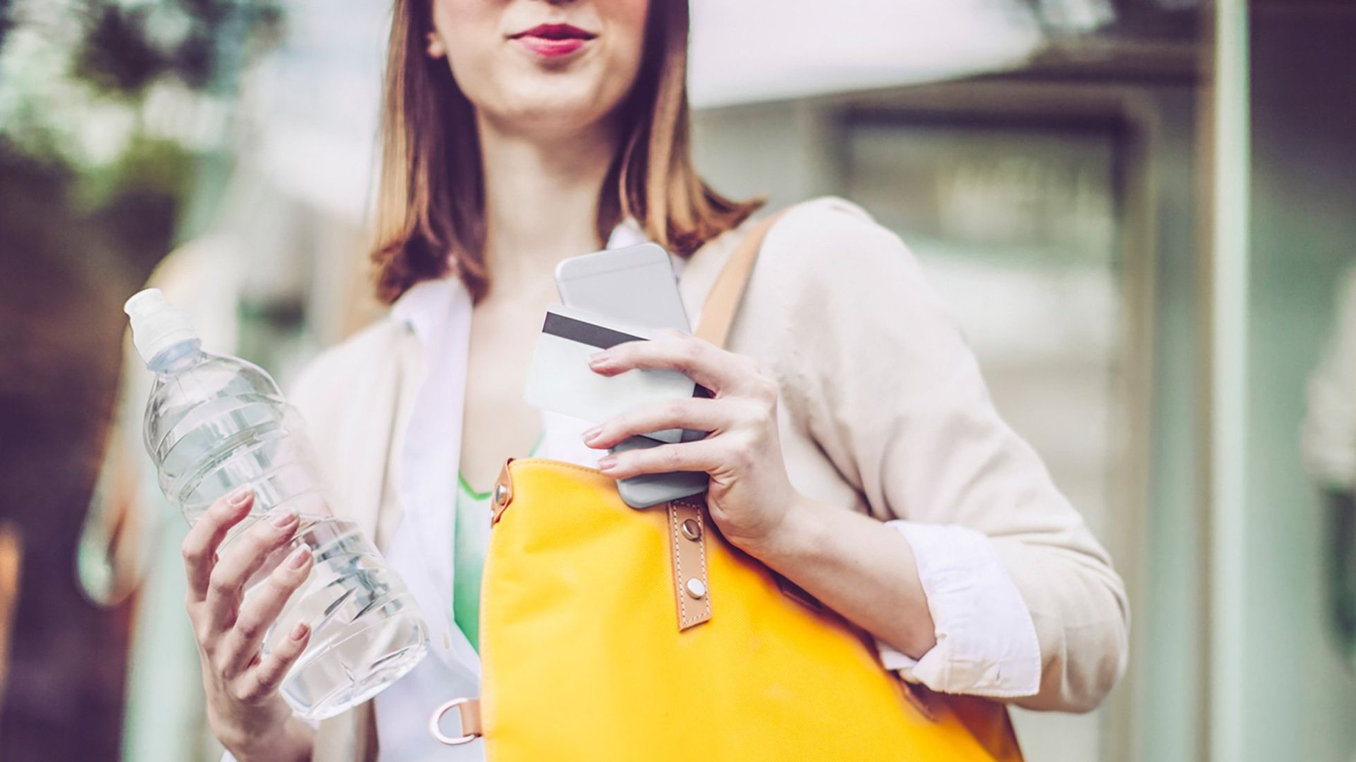 Woman holding a water bottle, smartphone, and yellow bag outdoors