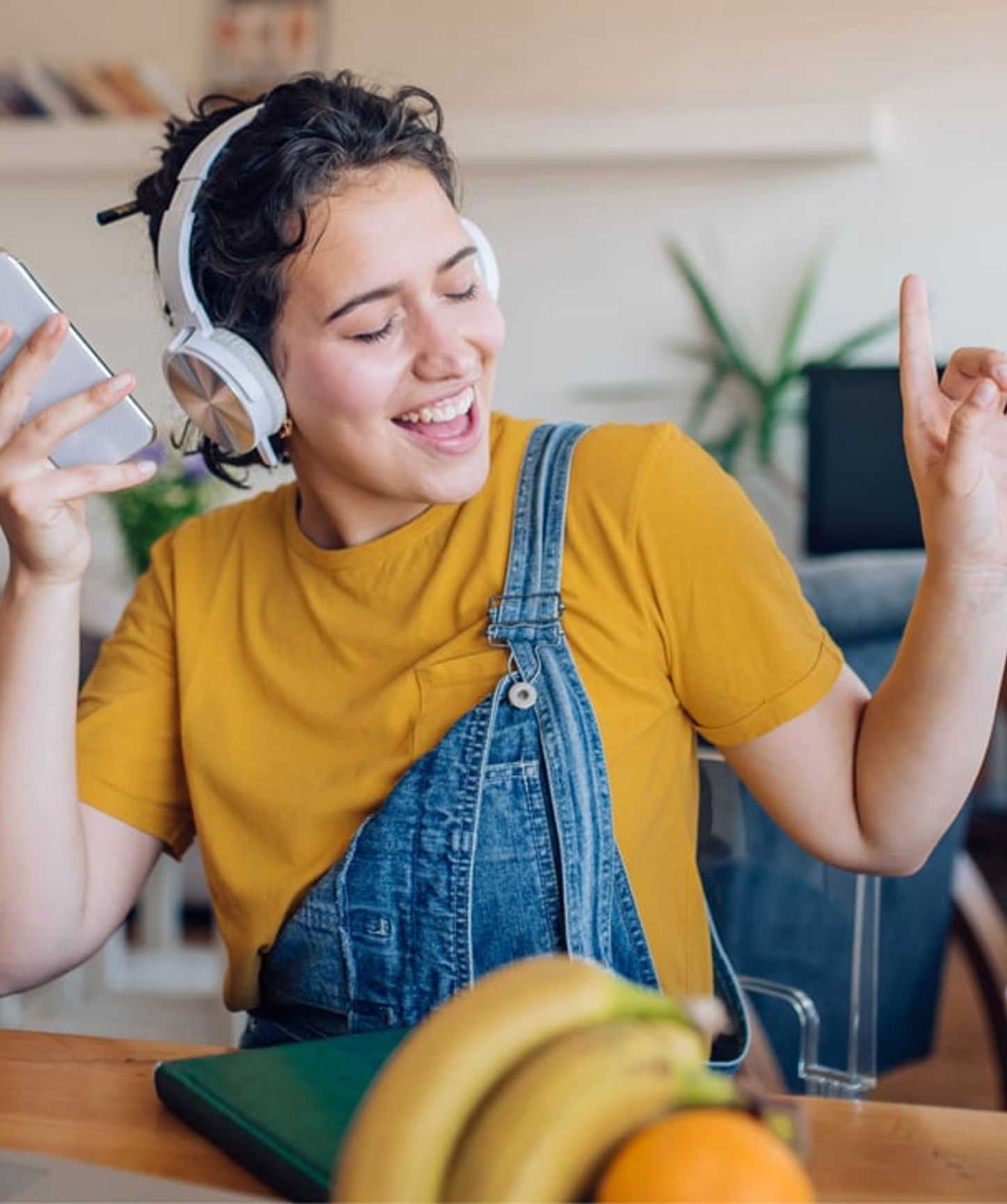 Young woman wearing headphones, joyfully listening to music and dancing while holding a smartphone.