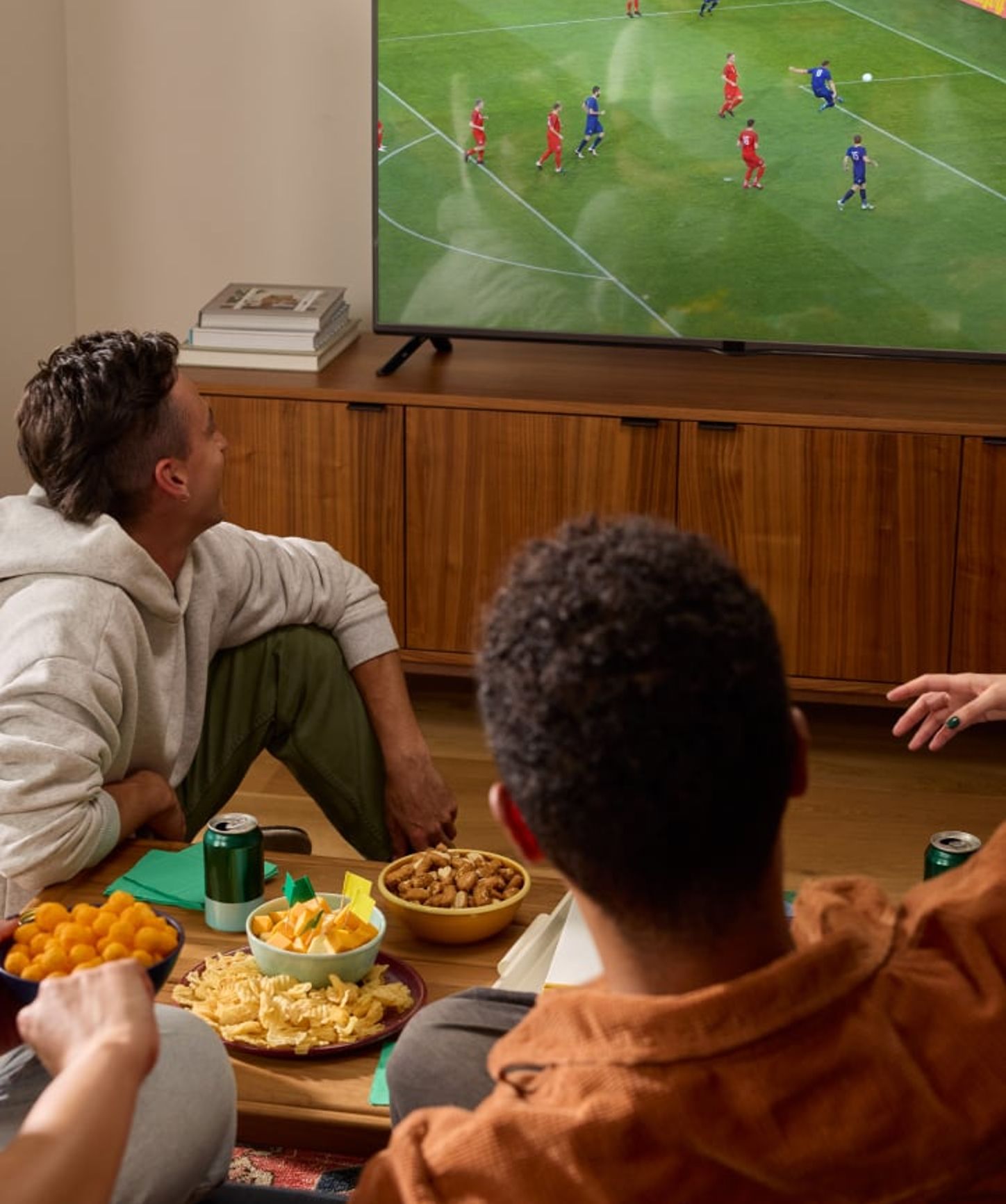 Friends gathered in a cozy living room, enjoying snacks and watching a soccer match on TV