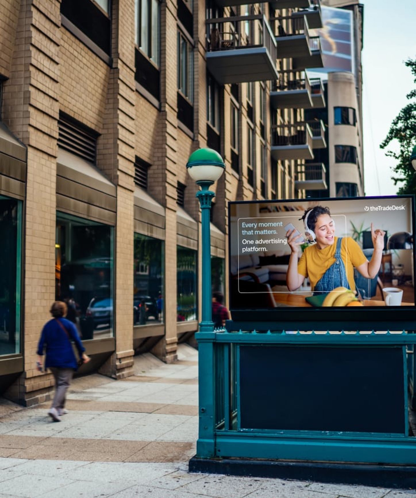 Urban street scene featuring a digital billboard advertisement for The Trade Desk, displaying a joyful woman listening to music