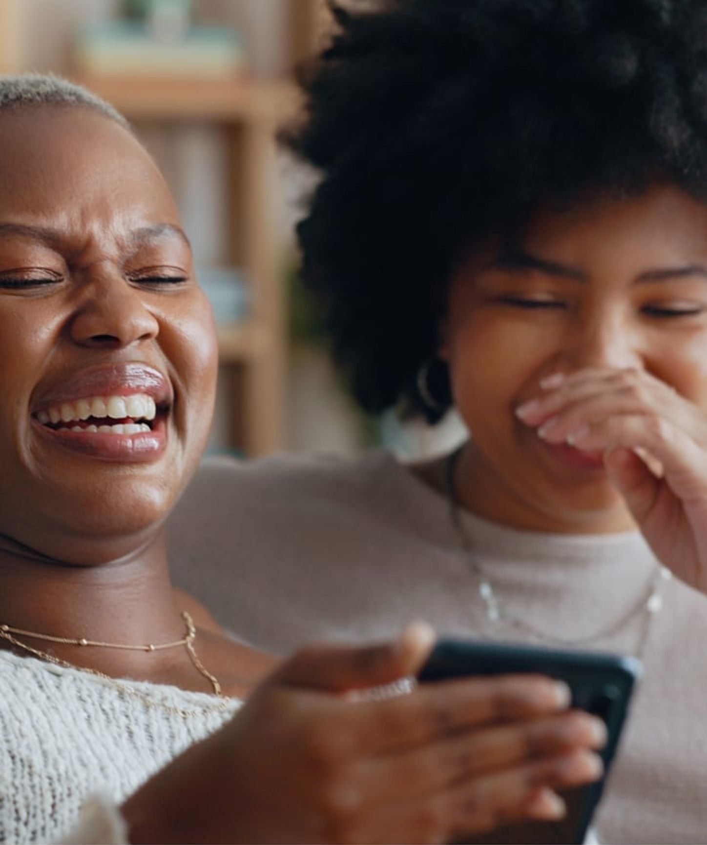 Two friends laughing together while looking at a smartphone, sharing a joyful moment