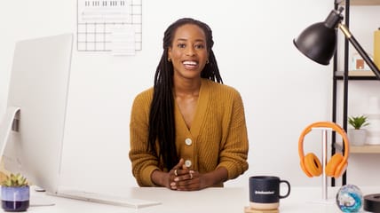 Image of a woman at a desk with a computer, while smiling and looking at the camera directly