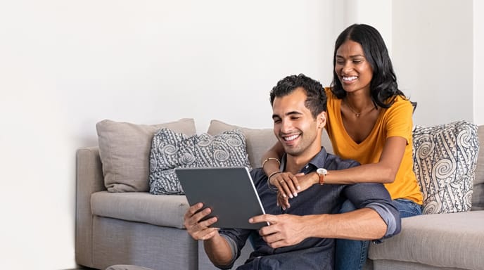 Couple sitting on a sofa, holding each other while on a tablet