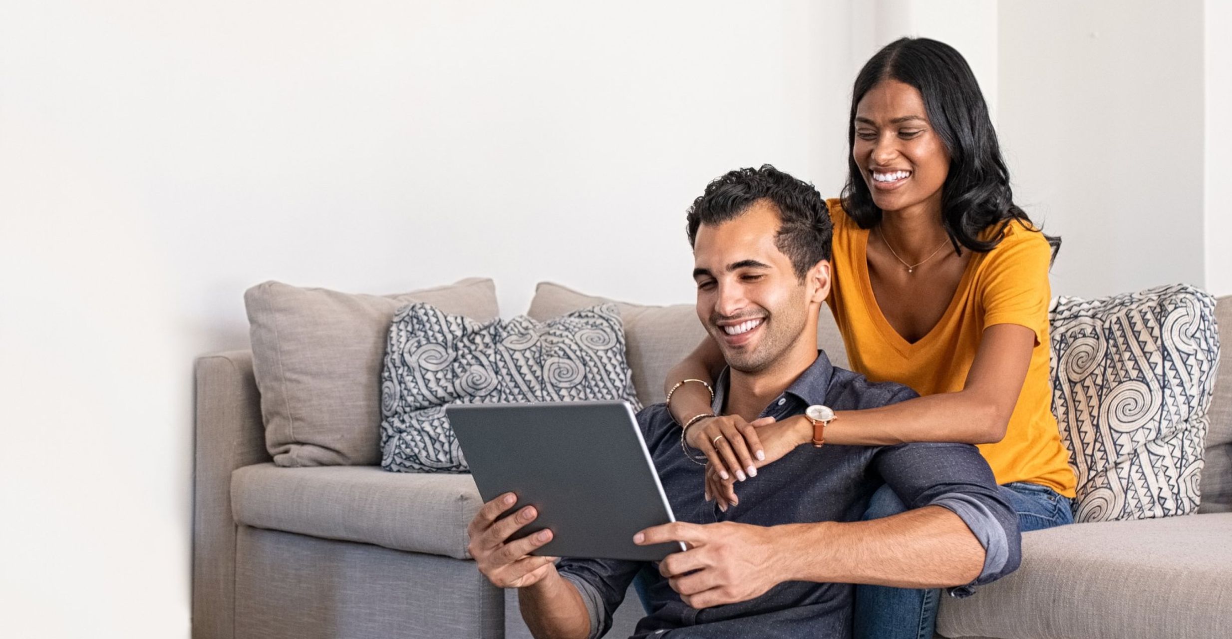 Couple sitting on a sofa, holding each other while on a tablet