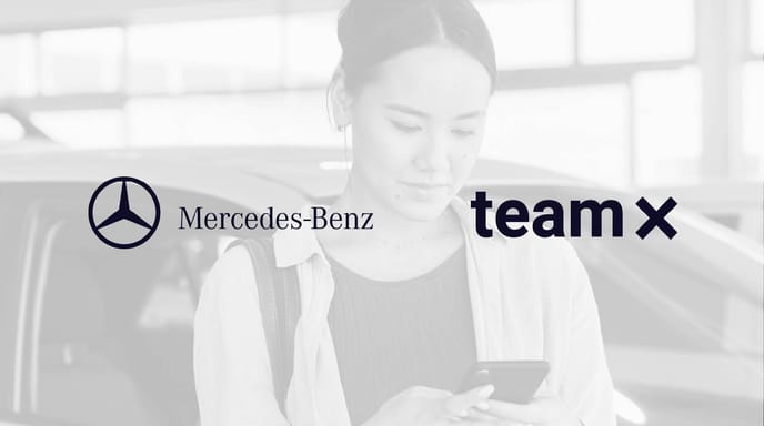 A woman stands next to a car looking at her phone in a showroom, overlaid with the Mercedes-Benz and Team X logos on a grayscale background.