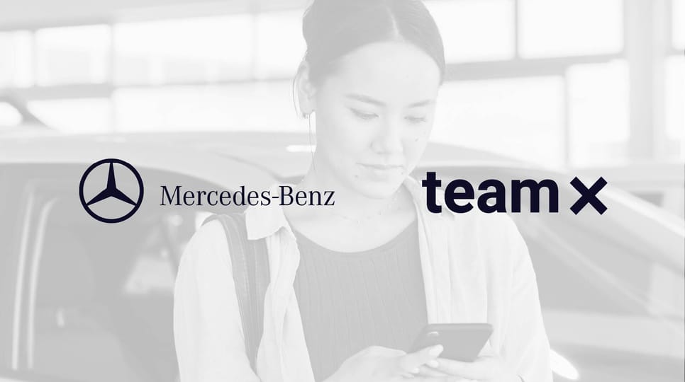 A woman stands next to a car looking at her phone in a showroom, overlaid with the Mercedes-Benz and Team X logos on a grayscale background.