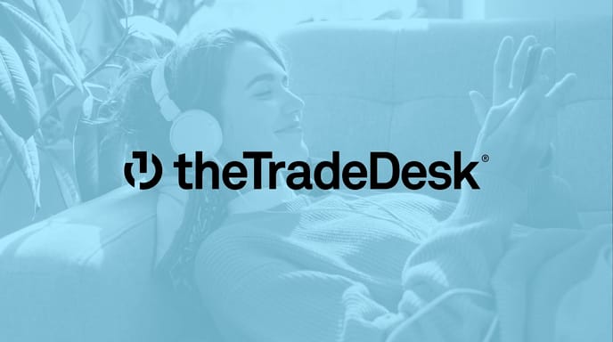 A woman relaxes on a couch wearing headphones and smiling at her phone, overlaid with The Trade Desk logo.