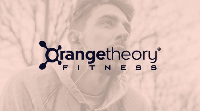 A man wearing a hoodie and earbuds pauses after a workout, overlaid with the Orangetheory Fitness logo.