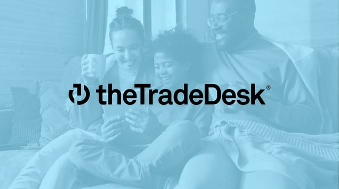 A mom, dad and child all holding each other and smiling while drinking coffees and looking at a tablet with a blue overlay and The Trade Desk logo in the center.