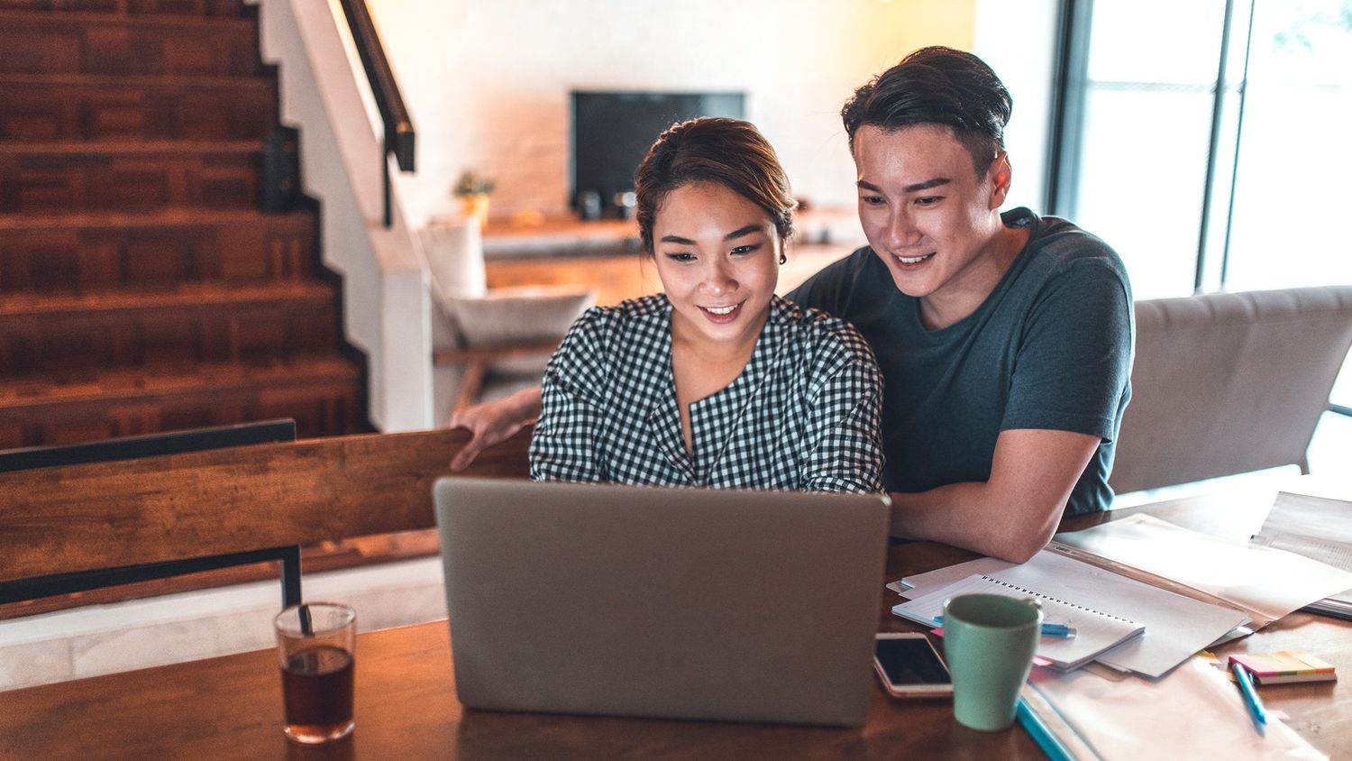 A happy couple works together on a laptop at a cozy home desk.