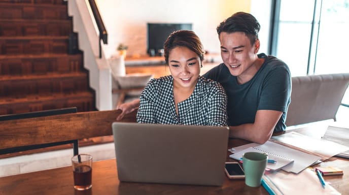 A happy couple works together on a laptop at a cozy home desk.