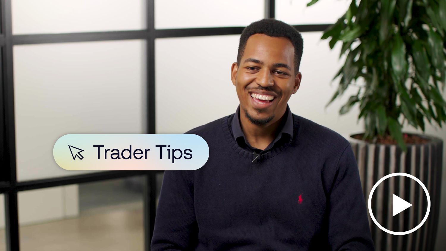 Man smiling in an office setting with a laptop on the desk and a plant in the background.