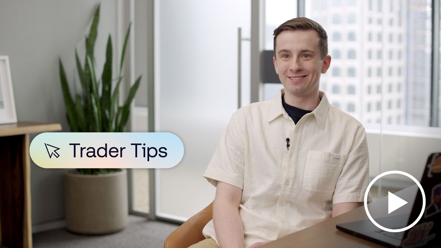 Candid image of a trader smiling at the camera while sitting at his desk with his laptop open. A banner on screen reads “Trader Tips."