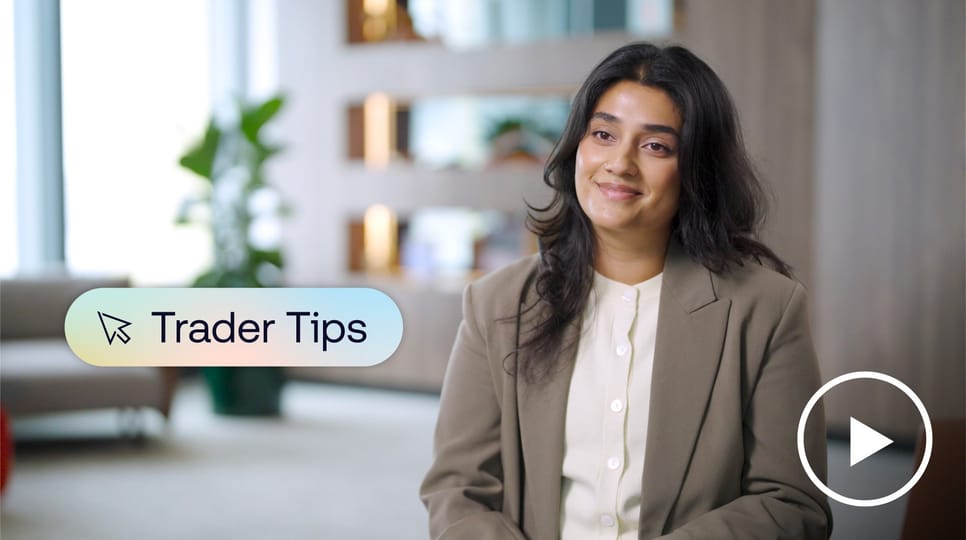 A woman in a beige blazer smiles in a modern office setting beside a graphic that reads 'Trader Tips' with a play button icon.