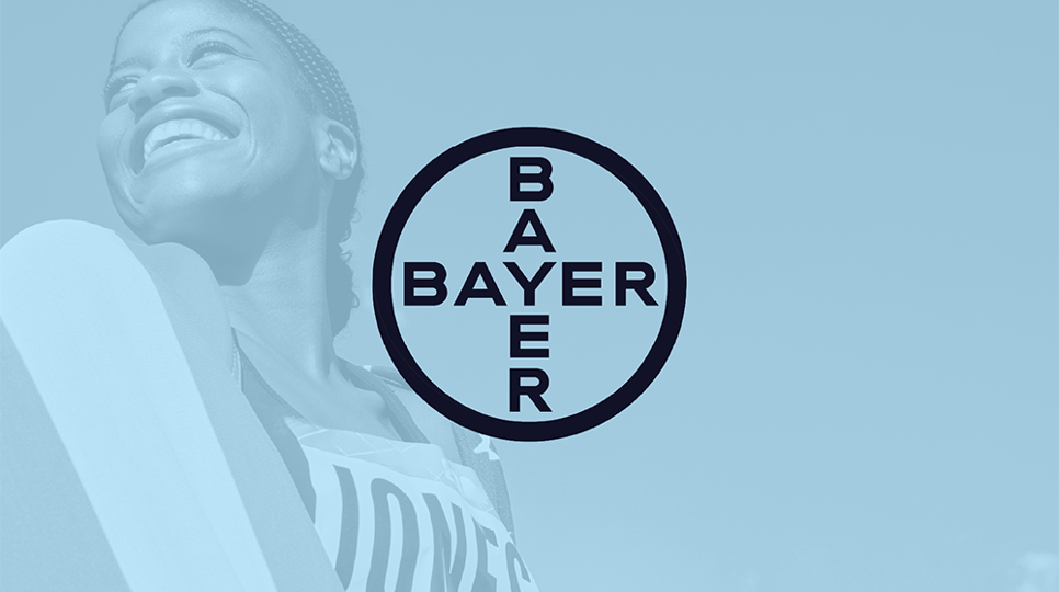 An olympian smiling and wrapped in the American flag with a blue overlay and the Bayer logo in the center