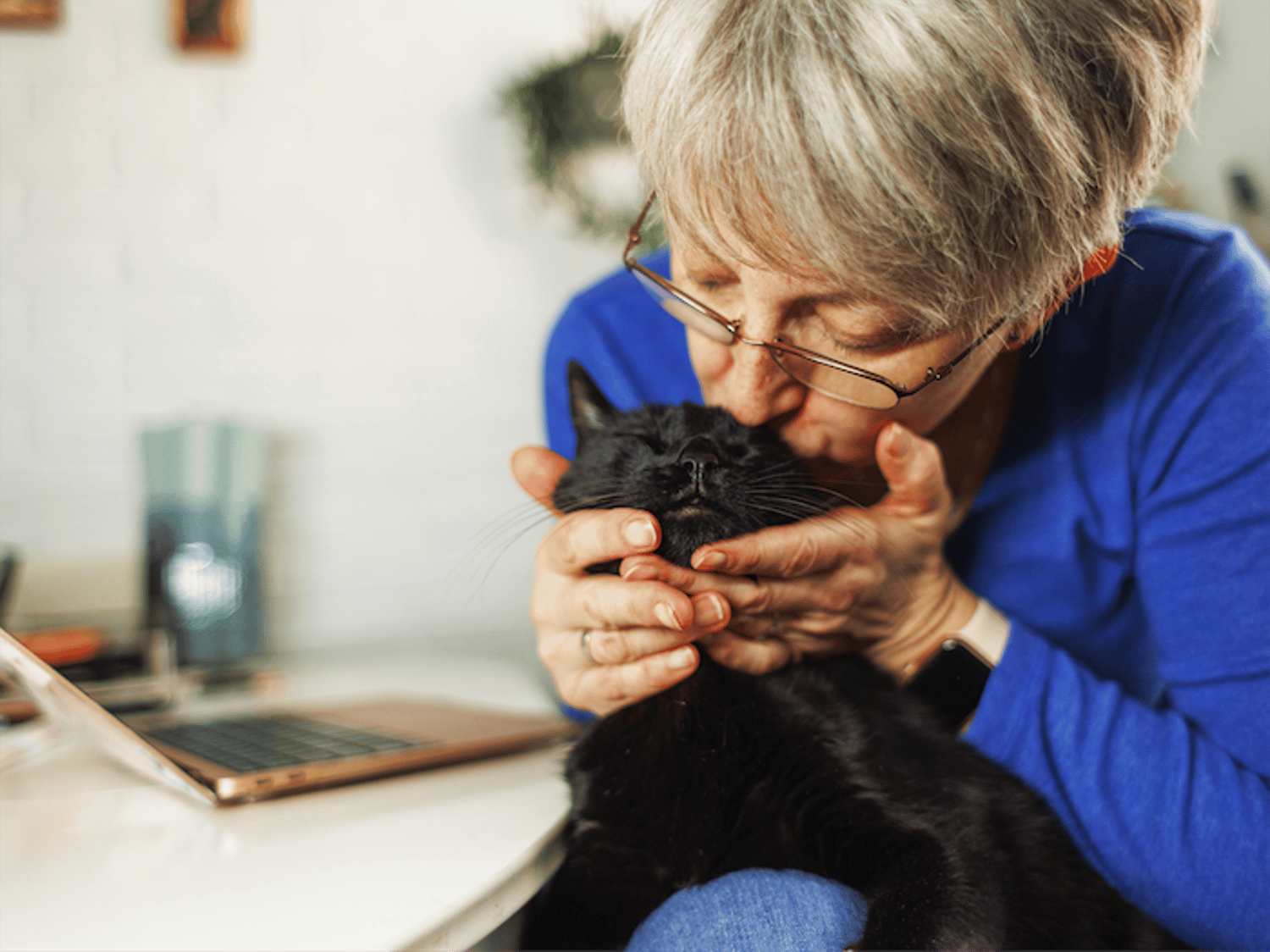 Image shows a woman kissing her black cat