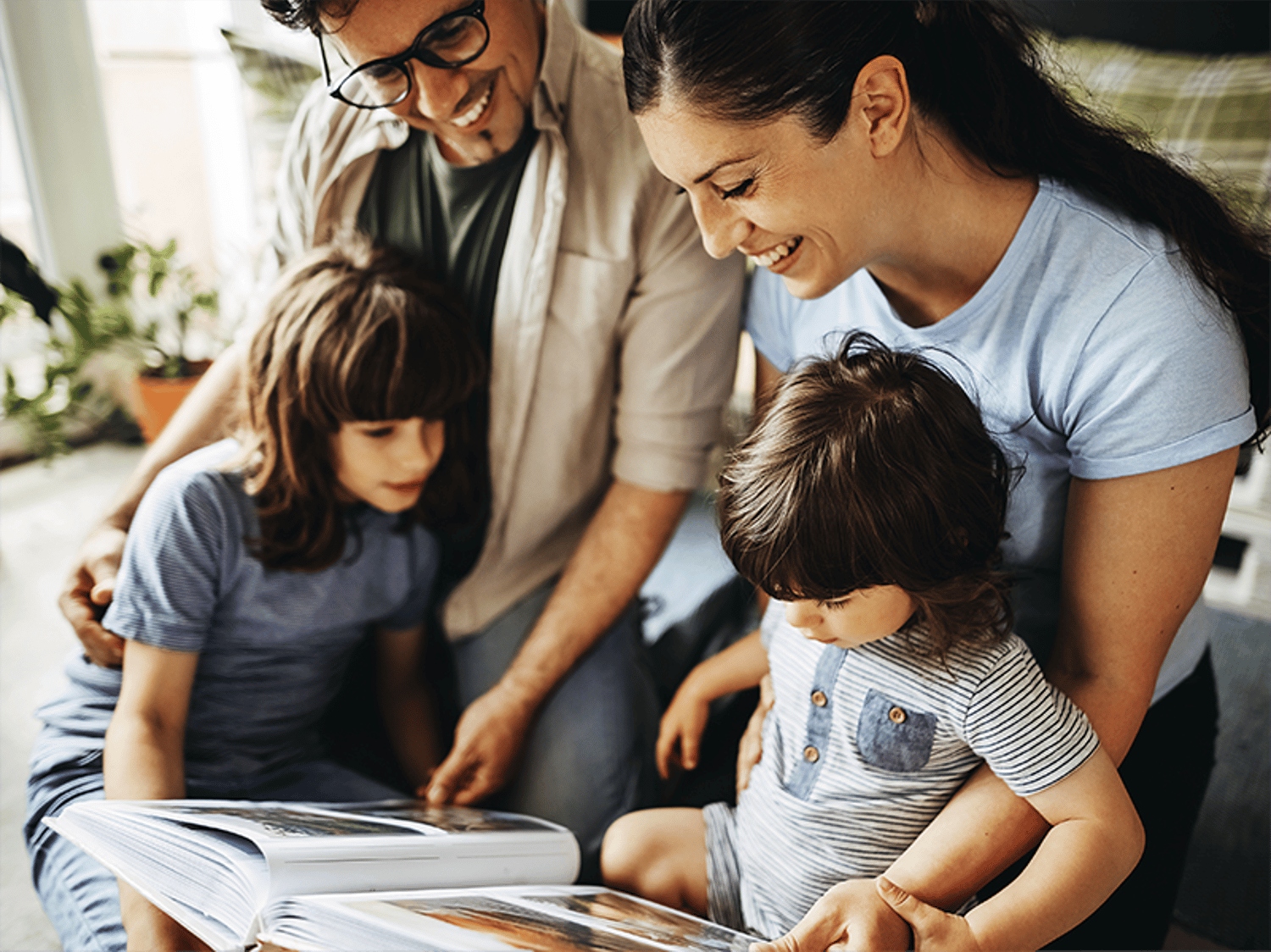 A happy family of four sitting together, smiling and looking at a book.