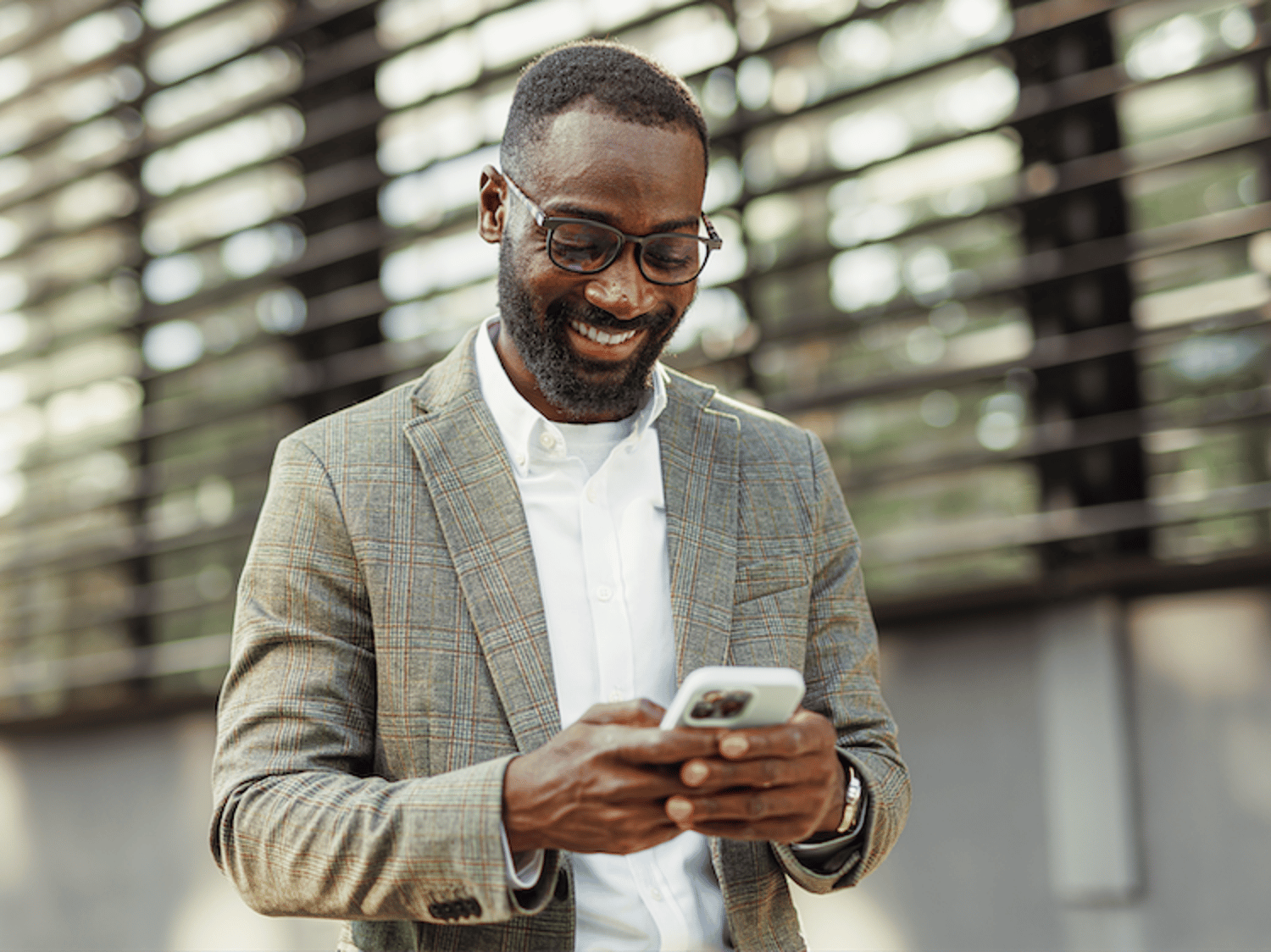 Image shows a man smiling and texting on his phone