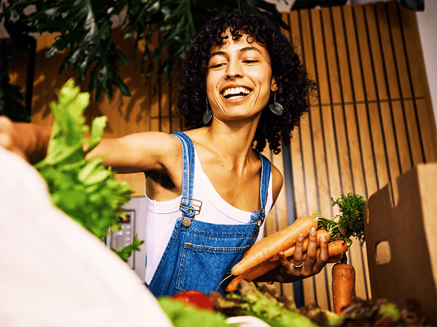Eine Frau in Latzhose, sie lacht und packt Gemüse aus