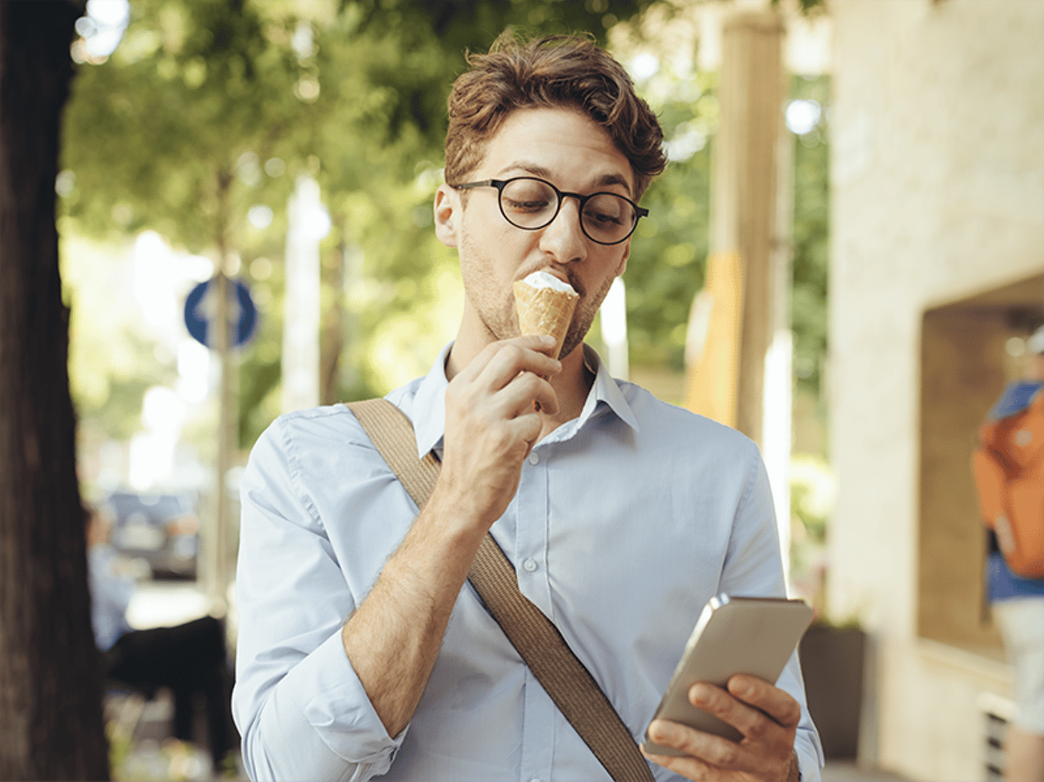 A man eating an ice cream cone while looking at his phone